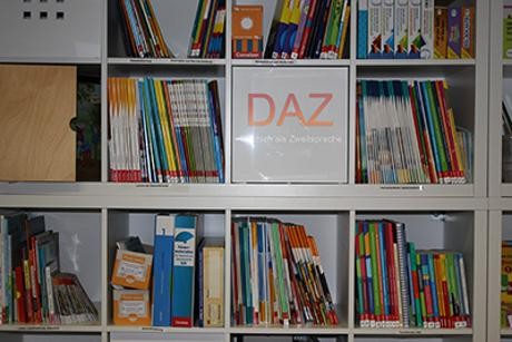 Foto aus dem Innentraum der DaZ-Mediathek mit dem Text: Lehrwerke, Fachliteratur, Spiele u. v. m. für Deutsch als Zweitsprache. Austausch, Beratung und Fortbildung